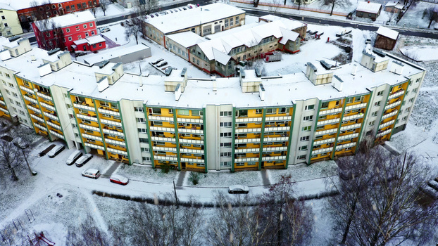 Aerial view of a curved multi story apartment building with yellow and green facades covered in a light dusting of snow surrounded by trees and a parking lot in Latvia. Aerial view of a curved multi story apartment building with yellow and green facades covered in a light dusting of snow surrounded by trees and a parking lot in Latvia.