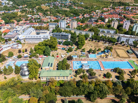 Aerial view of crowded outdoor thermal pools waterslides and spa buildings beside leafy urban neighborhoods in Eger Hungary during summer recreation. Aerial view of crowded outdoor thermal pools waterslides and spa buildings beside leafy urban neighborhoods in Eger Hungary during summer recreation.