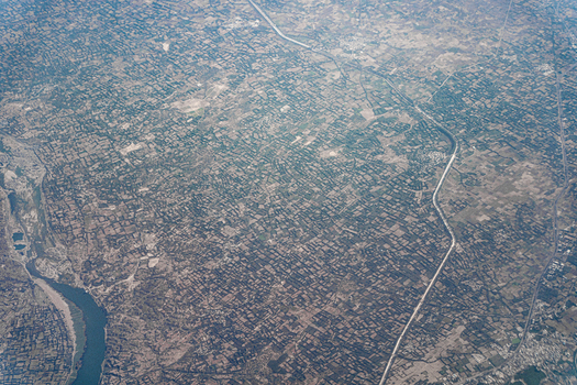 Aerial view of a vast agricultural landscape with a dense grid of farm plots a winding river and a long straight canal under a hazy sky in India. Aerial view of a vast agricultural landscape with a dense grid of farm plots a winding river and a long straight canal under a hazy sky in India.