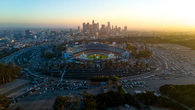Aerial view of Dodger Stadium surrounded by cars glows under a soft sunset sky against the backdrop of the Los Angeles skyline Los Angeles California United States. Aerial view of Dodger Stadium surrounded by cars glows under a soft sunset sky against the backdrop of the Los Angeles skyline Los Angeles California United States.