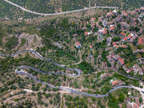 Aerial view of the historic stone houses and terracotta roofs of a hillside village with a winding mountain road and lush green vegetation in Qeparo Fshat Vlore County Albania. Aerial view of the historic stone houses and terracotta roofs of a hillside village with a winding mountain road and lush green vegetation in Qeparo Fshat Vlore County Albania.