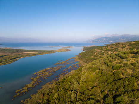 Aerial view of Kanali i Vivarit with its blue waters flowing between lush green hills and wetlands under a clear sky in Vrine Vlore County Albania. Aerial view of Kanali i Vivarit with its blue waters flowing between lush green hills and wetlands under a clear sky in Vrine Vlore County Albania.