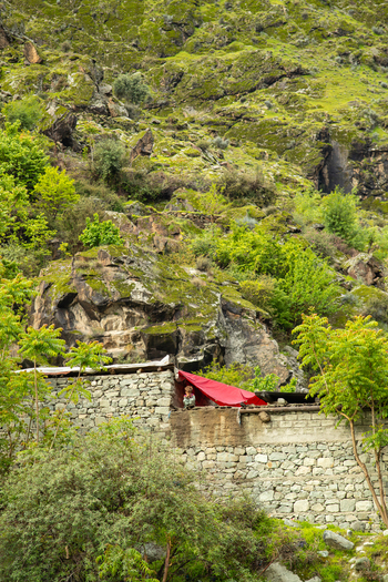 View of a traditional stone building with a red tarp on a lush green rocky hillside in Chilas Gilgit Pakistan. View of a traditional stone building with a red tarp on a lush green rocky hillside in Chilas Gilgit Pakistan.