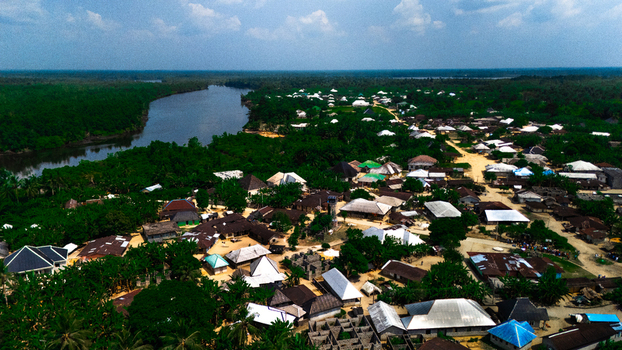 Aerial view of the village of Abua nestled among lush tropical vegetation and bordering a winding river with traditional houses and dirt paths in Abua Rivers Nigeria. Aerial view of the village of Abua nestled among lush tropical vegetation and bordering a winding river with traditional houses and dirt paths in Abua Rivers Nigeria.