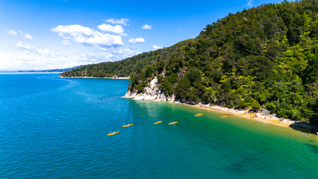 Aerial view of kayaks float on turquoise waters near lush green cliffs Abel Tasman National Park Tasman Region New Zealand. Aerial view of kayaks float on turquoise waters near lush green cliffs Abel Tasman National Park Tasman Region New Zealand.