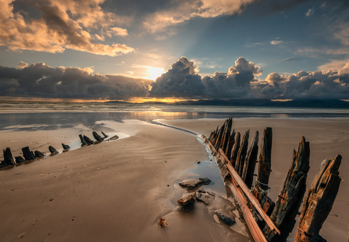 View of the weathered wooden remains of a shipwreck on the wet sand under a dramatic sunset sky with golden light and heavy clouds Inch Beach County Kerry Ireland. View of the weathered wooden remains of a shipwreck on the wet sand under a dramatic sunset sky with golden light and heavy clouds Inch Beach County Kerry Ireland.