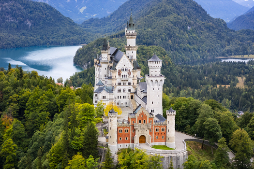 Aerial view of Neuschwanstein Castle perched atop a hill a fairy tale fortress against a backdrop of lush forests and serene blue lakes Schwangau Bayern Germany. Aerial view of Neuschwanstein Castle perched atop a hill a fairy tale fortress against a backdrop of lush forests and serene blue lakes Schwangau Bayern Germany.