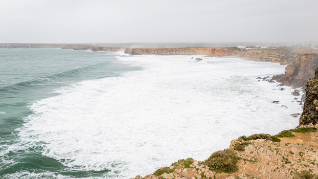 Aerial view of the rugged cliffs of Sagres with powerful waves crashing against the rocky shore under a misty sky in Sagres Faro Portugal. Aerial view of the rugged cliffs of Sagres with powerful waves crashing against the rocky shore under a misty sky in Sagres Faro Portugal.