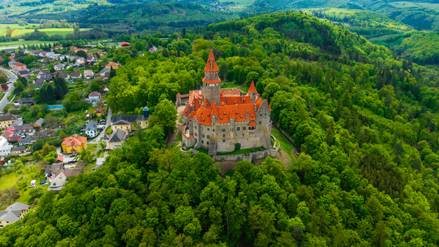 Aerial view of Bouzov Castle with its iconic red rooftops and stone towers nestled in a lush green forest under a bright sky in Bouzov Olomoucky kraj Czechia. Aerial view of Bouzov Castle with its iconic red rooftops and stone towers nestled in a lush green forest under a bright sky in Bouzov Olomoucky kraj Czechia.