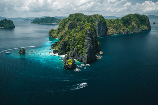 Aerial view of limestone cliffs rising from turquoise waters with traditional outrigger boats anchored near the shore in El Nido Mimaropa Philippines. Aerial view of limestone cliffs rising from turquoise waters with traditional outrigger boats anchored near the shore in El Nido Mimaropa Philippines.