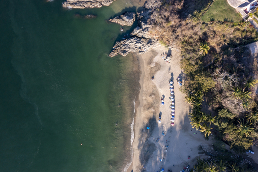 Aerial view of the sandy beach in Sayulita with colorful umbrellas palm trees and rocky coastline meeting the turquoise ocean water in Sayulita Nayarit Mexico. Aerial view of the sandy beach in Sayulita with colorful umbrellas palm trees and rocky coastline meeting the turquoise ocean water in Sayulita Nayarit Mexico.