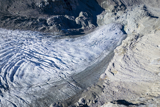 Aerial view of the textured icy expanse of Morteratsch Glacier snaking through the rugged rocky terrain contrasting starkly against the pale landscape Morteratsch Glacier Grisons Switzerland. Aerial view of the textured icy expanse of Morteratsch Glacier snaking through the rugged rocky terrain contrasting starkly against the pale landscape Morteratsch Glacier Grisons Switzerland.