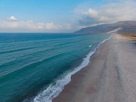 Aerial view of the turquoise sea meeting the sandy shore under a soft sky near the rugged mountains Ararhin Socotra Yemen. Aerial view of the turquoise sea meeting the sandy shore under a soft sky near the rugged mountains Ararhin Socotra Yemen.
