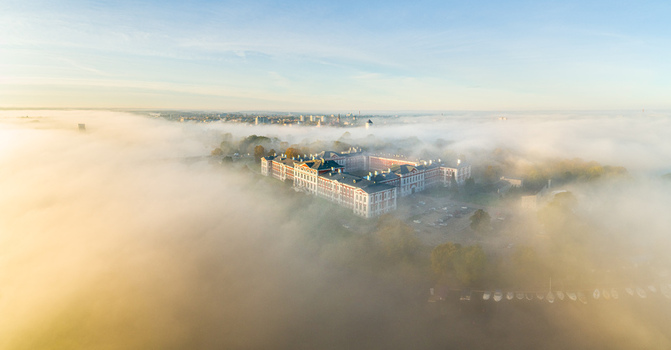 Aerial view of Jelgava Palace emerging from thick morning fog with soft golden light illuminating the historic architecture and surrounding landscape in Jelgava Latvia. Aerial view of Jelgava Palace emerging from thick morning fog with soft golden light illuminating the historic architecture and surrounding landscape in Jelgava Latvia.