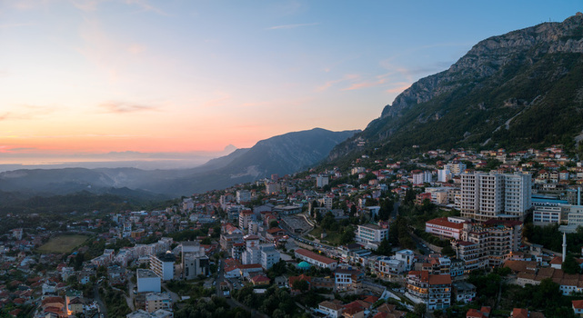 Aerial view of the town of Kruje nestled at the foot of a rugged mountain under a soft sunset sky with urban buildings and rooftops Kruje Durres County Albania.