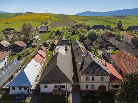 Aerial view of traditional houses with steep roofs and green gardens with yellow fields and mountains in the distance Partizanska Lupca Zilina Region Slovakia.