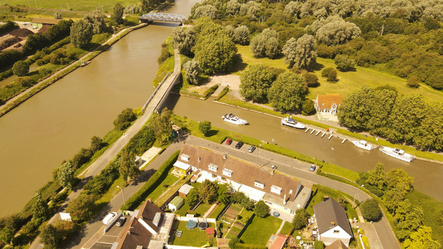 Aerial view of the canal in Saint Omer featuring boats moored along the bank a bridge crossing the water and residential houses with green gardens in Saint Omer Hauts de France France. Aerial view of the canal in Saint Omer featuring boats moored along the bank a bridge crossing the water and residential houses with green gardens in Saint Omer Hauts de France France.