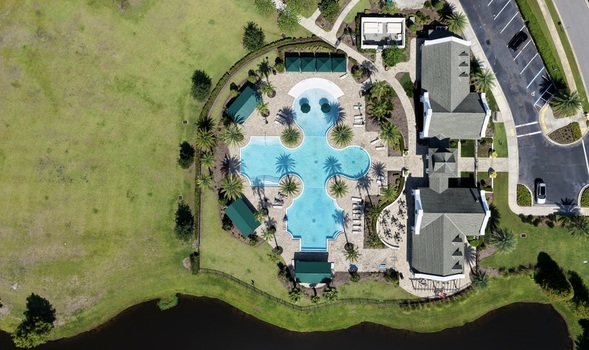 Aerial view of the Windward Ranch swimming pool complex featuring a uniquely shaped pool surrounding palm trees clubhouse and green lawns in St. Johns County Florida United States. Aerial view of the Windward Ranch swimming pool complex featuring a uniquely shaped pool surrounding palm trees clubhouse and green lawns in St. Johns County Florida United States.