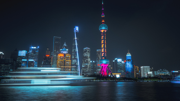 View of the North Bund and illuminated Shanghai skyline at night featuring the Oriental Pearl Tower and light trails from a boat on the Huangpu River in Shanghai Shanghai China.