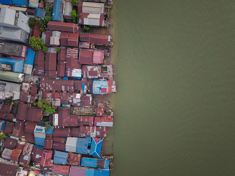 Aerial view of Mahakam River flowing past a dense settlement of colorful houses with corrugated metal roofs in Samarinda East Kalimantan Indonesia. Aerial view of Mahakam River flowing past a dense settlement of colorful houses with corrugated metal roofs in Samarinda East Kalimantan Indonesia.