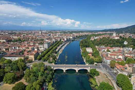 Aerial view of the Po River flowing through the city center with the Mole Antonelliana spire and historic bridges under a blue sky in Turin Piedmont Italy.