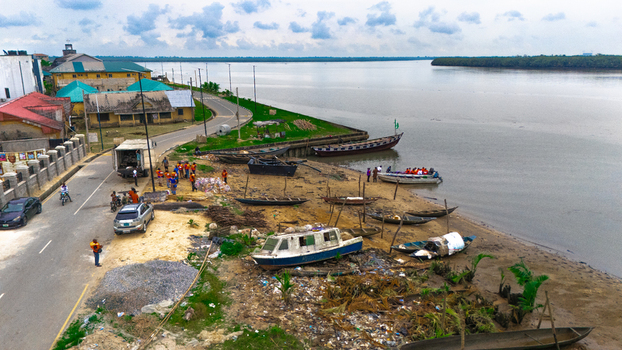 Aerial view of a riverbank with wooden boats small motorboats and people gathered near a road with buildings and vegetation along the shore in Minima Rivers Nigeria.