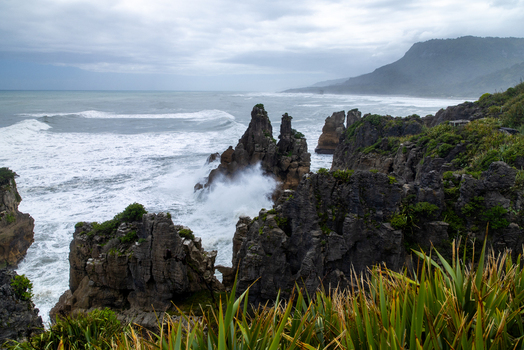 View of waves crashing against the rugged dark rock formations along the coastline under a cloudy sky Pancake Rocks and Blowholes Walk West Coast Region New Zealand. View of waves crashing against the rugged dark rock formations along the coastline under a cloudy sky Pancake Rocks and Blowholes Walk West Coast Region New Zealand.