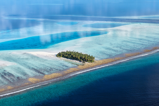 Aerial view of lush tropical islands with green palm trees and turquoise coral reefs surrounded by the deep blue ocean under a clear sky near Vaanee Dhaalu Atoll Maldives. Aerial view of lush tropical islands with green palm trees and turquoise coral reefs surrounded by the deep blue ocean under a clear sky near Vaanee Dhaalu Atoll Maldives.