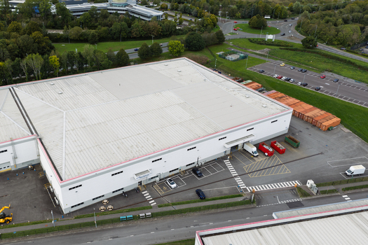 Aerial view of a large white data center building with a flat roof surrounded by parking areas access roads and green landscaping in United Kingdom.