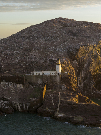 Aerial view of Bass Rock Lighthouse on the steep cliffs of the volcanic island under warm sunset light North Berwick Scotland United Kingdom. Aerial view of Bass Rock Lighthouse on the steep cliffs of the volcanic island under warm sunset light North Berwick Scotland United Kingdom.