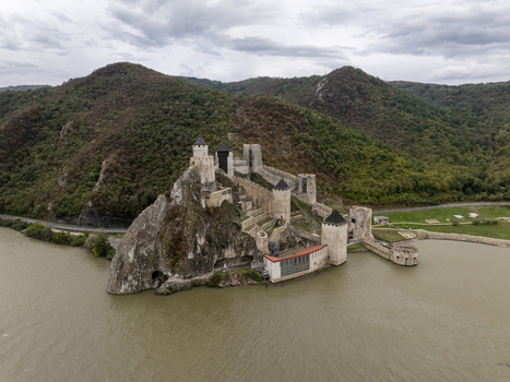 Aerial view of Golubac Fortress perched on a rocky cliff overlooking the Danube River surrounded by lush green hills under a cloudy sky Golubac Branicevski Okrug Serbia. Aerial view of Golubac Fortress perched on a rocky cliff overlooking the Danube River surrounded by lush green hills under a cloudy sky Golubac Branicevski Okrug Serbia.