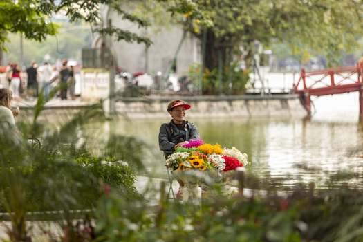 Hanoi Ha Noi Vietnam 11 November 2025 View of a flower seller sitting on a bicycle with colorful bouquets near the iconic red Huc Bridge at Hoan Kiem Lake.