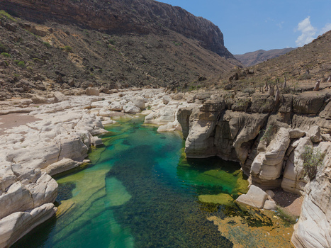Aerial view of the turquoise river snaking through the stark sun baked rocks of Kalysan Canyon a hidden oasis framed by towering cliffs Kalysan Socotra Yemen. Aerial view of the turquoise river snaking through the stark sun baked rocks of Kalysan Canyon a hidden oasis framed by towering cliffs Kalysan Socotra Yemen.