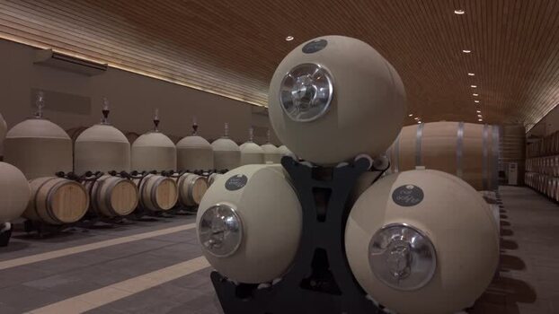 Rows of wooden barrels and spherical containers fill the dimly lit cellar creating a sense of depth and texture