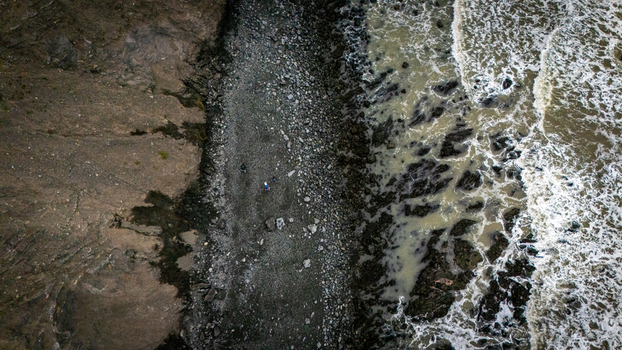 Aerial view of the rugged Lost Coast shoreline featuring a rocky beach with crashing waves and small figures walking along the coast in Humboldt County California United States.