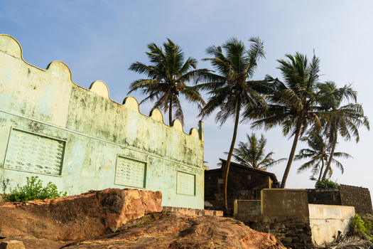 View of a weathered light green building with a scalloped roofline and palm trees against a clear blue sky in Galle Southern Province Sri Lanka.