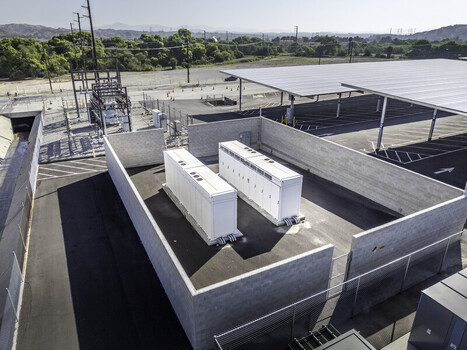 Aerial view of industrial battery energy storage units enclosed by a concrete wall next to solar panel carports and electrical infrastructure Los Angeles County California United States. Aerial view of industrial battery energy storage units enclosed by a concrete wall next to solar panel carports and electrical infrastructure Los Angeles County California United States.