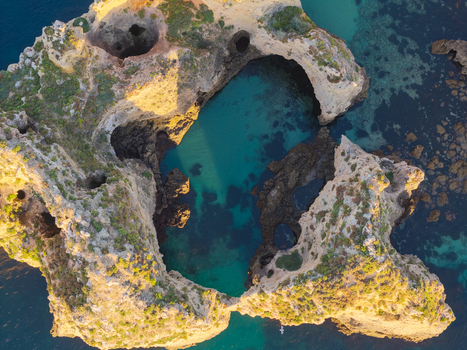 Aerial view of the dramatic limestone cliffs and sea caves of Ponta da Piedade with turquoise water and golden sunlight in Lagos Faro District Portugal.