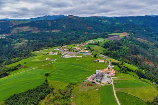 Aerial view of a small rural village nestled among lush green rolling hills and agricultural fields under a cloudy sky in Cudillero Asturias Spain.