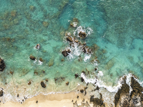 Aerial view of Waikoloa Beach featuring turquoise ocean water crashing against dark volcanic rocks and a sandy shoreline Waikoloa Village Hawaii United States.