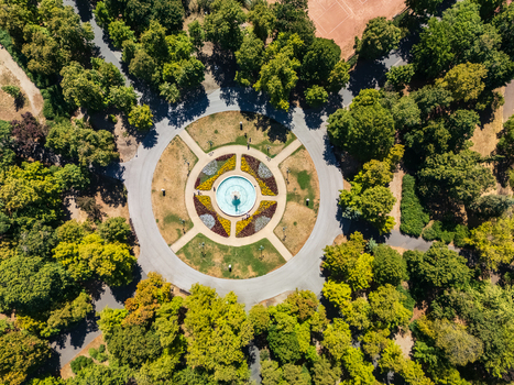 Aerial view of a circular fountain geometric flower beds and tree lined paths in a public park with a nearby tennis court in Eger Hungary during summer. Aerial view of a circular fountain geometric flower beds and tree lined paths in a public park with a nearby tennis court in Eger Hungary during summer.