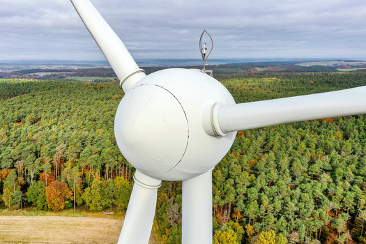 Aerial view of a wind turbine hub and blades overlooking a vast forest with autumn colors under a cloudy sky in Simmerath Nordrhein Westfalen Germany. Aerial view of a wind turbine hub and blades overlooking a vast forest with autumn colors under a cloudy sky in Simmerath Nordrhein Westfalen Germany.