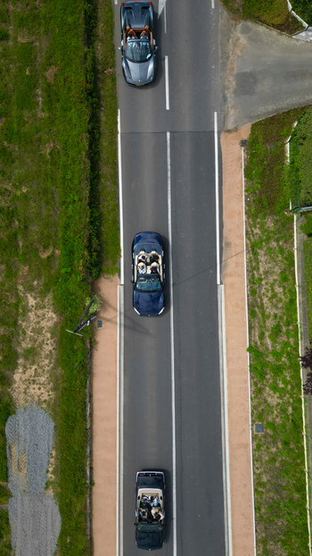 Aerial view of three convertible cars with people inside driving along a paved road bordered by green grass and vegetation in La Chapelle de Guinchay Bourgogne Franche Comte France.