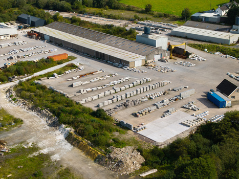 Aerial view of a stone and concrete supply yard featuring rows of stacked building materials a large industrial warehouse and surrounding green fields in Lisburn Northern Ireland United Kingdom. Aerial view of a stone and concrete supply yard featuring rows of stacked building materials a large industrial warehouse and surrounding green fields in Lisburn Northern Ireland United Kingdom.