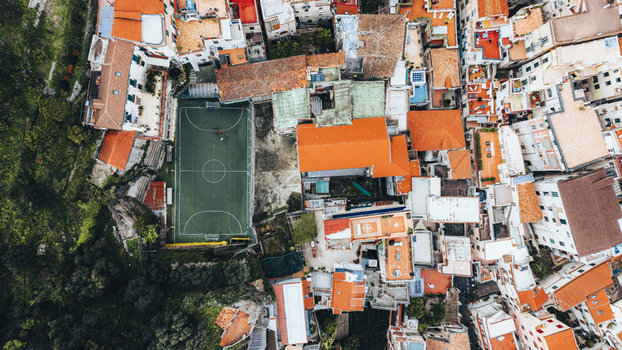 Aerial view of colorful buildings with red roofs clustered around a vibrant green football field nestled beside a dark green forest Amalfi Italy. Aerial view of colorful buildings with red roofs clustered around a vibrant green football field nestled beside a dark green forest Amalfi Italy.