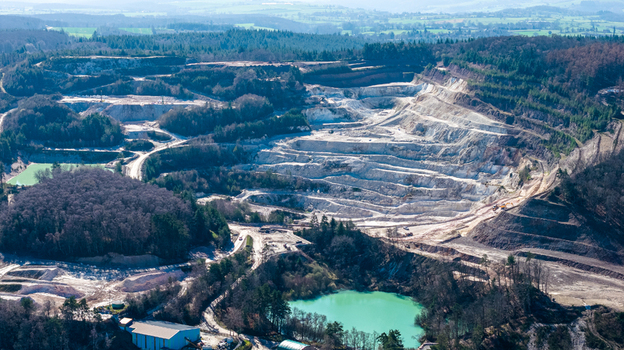Aerial view of a vast quarry carved into the earth contrasting with the surrounding dense forest and tranquil blue waters &Eacute;chassi&egrave;res Auvergne Rh&ocirc;ne Alpes France.