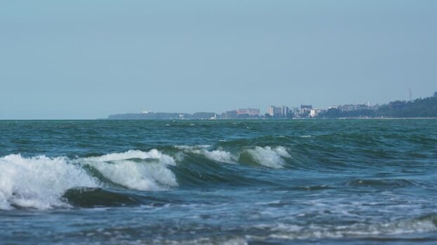 View of waves crashing on the shore with city skyline Bangladesh.