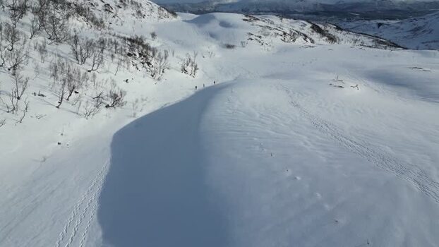 Aerial view of people hiking on snowy Kvaloya mountains Norway.