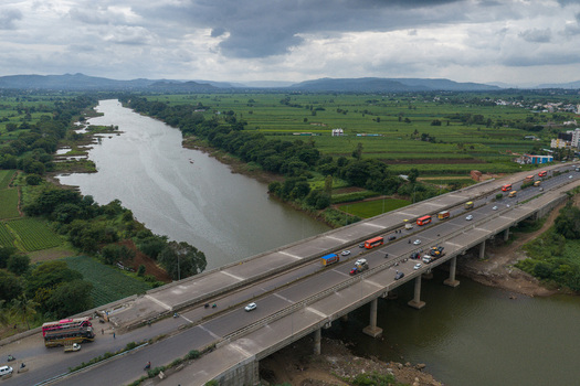Aerial view of a highway bridge crossing a river with traffic surrounded by lush green agricultural fields under a cloudy sky in Karad Maharashtra India.