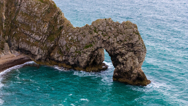 Aerial view of Durdle Door a natural limestone arch on the Jurassic Coast with turquoise sea waves crashing against the rocky cliffs in Wareham England United Kingdom. Aerial view of Durdle Door a natural limestone arch on the Jurassic Coast with turquoise sea waves crashing against the rocky cliffs in Wareham England United Kingdom.